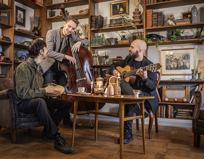 Bild på Fred Holmlund Trio, tre män som sitter i ett vardagsrum runt ett bord